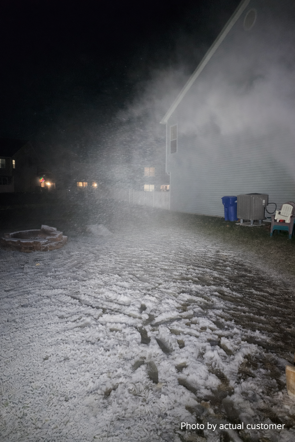 Snowmaker blasting snow across a backyard at night