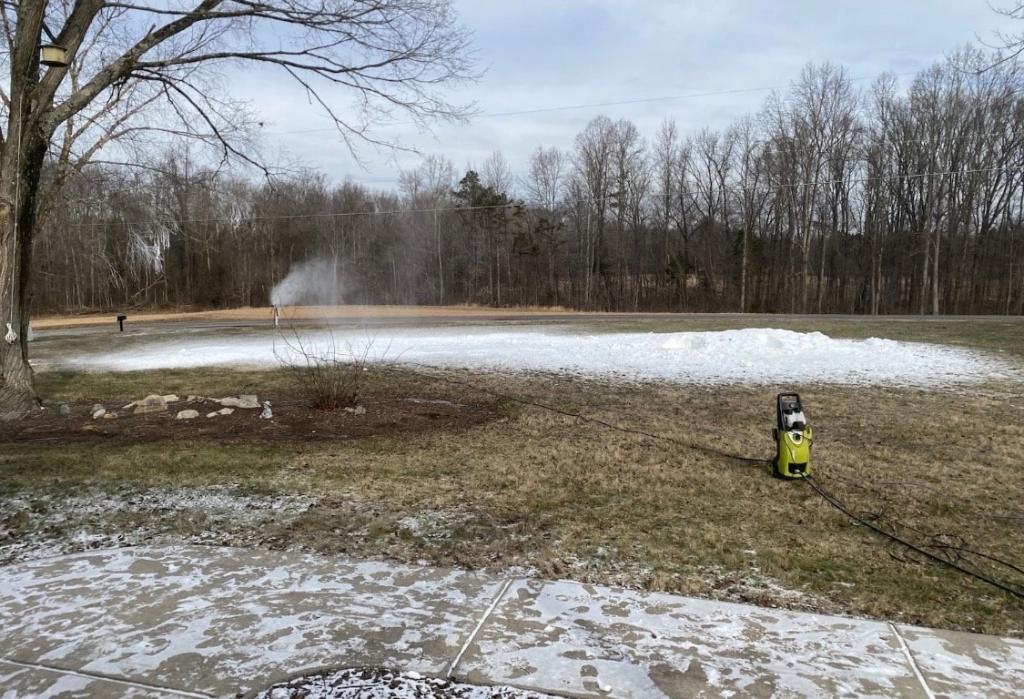 Snowmaker running in a backyard field with a pile of snow building up